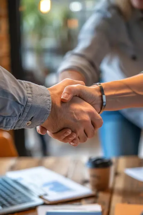 Deux personnes se serrent la main lors d'un accord professionnel, avec un ordinateur portable et des documents sur la table.